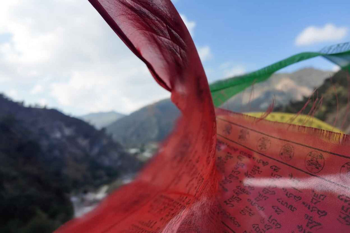 A prayer flag fluttering against a mountain valley, representing Tribal Sangha's sourcing from sangha farms in the Himalayas and Western Ghats